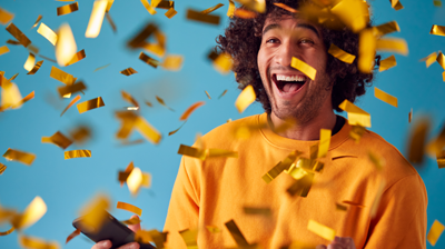 Celebrating Young Man With Mobile Phone Winning Prize And Showered With Gold Confetti In Studio