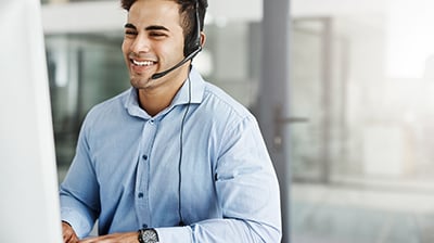 A man wearing a headset and smiling while working on his computer 